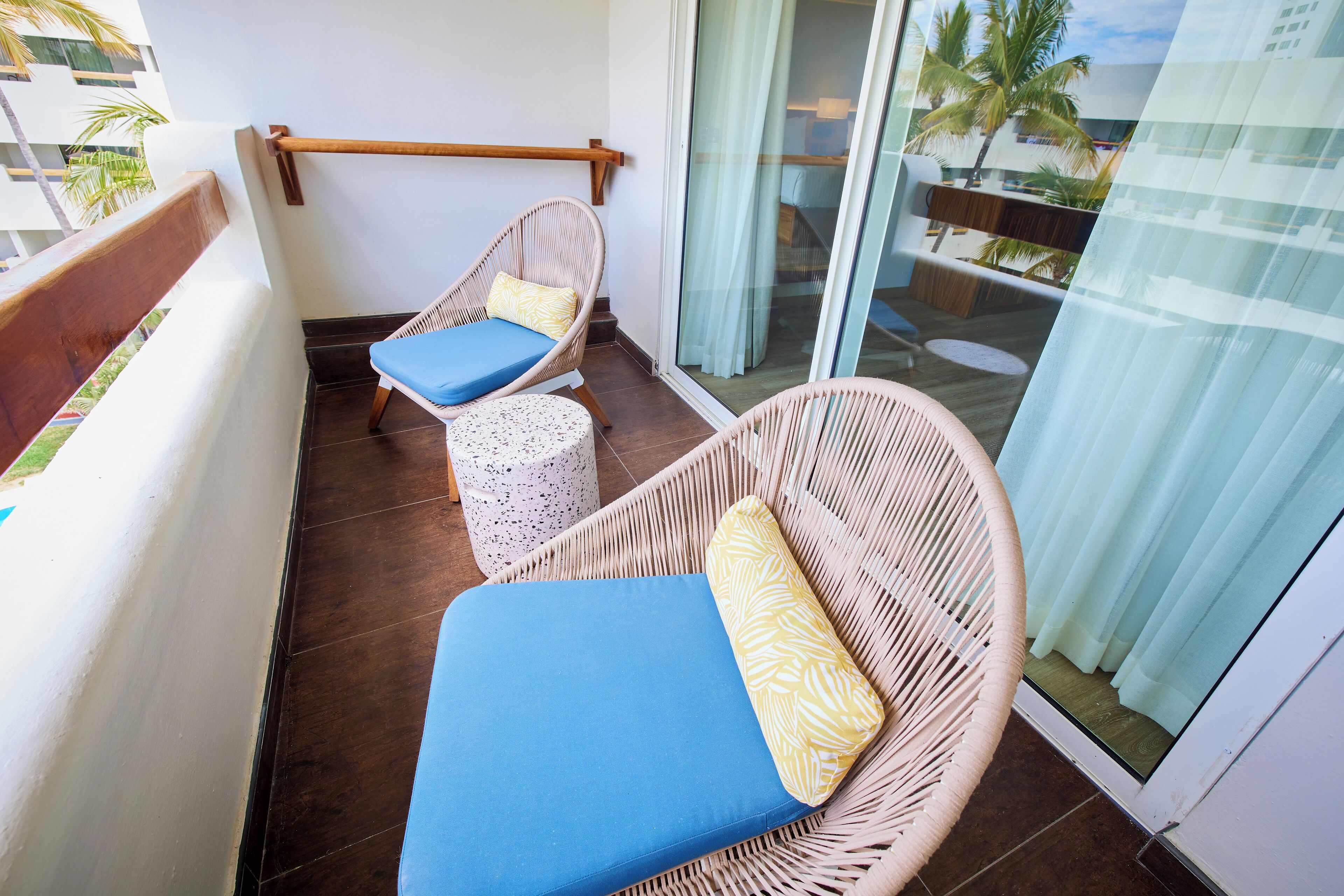 A balcony with wicker furniture, including two chairs and a small table, and a glass door leading to a pool area.