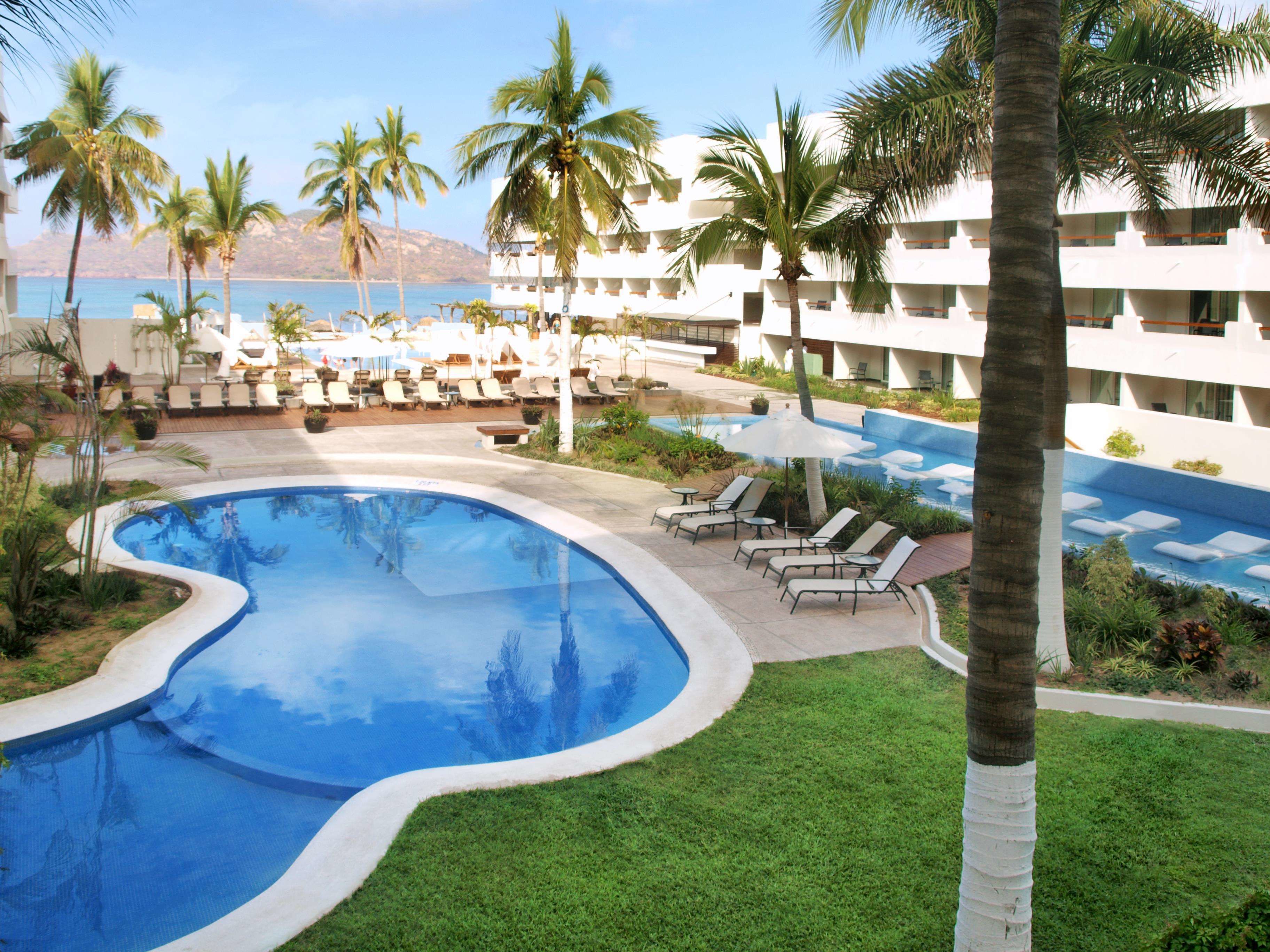A resort pool with palm trees, lounge chairs, and a view of the ocean.