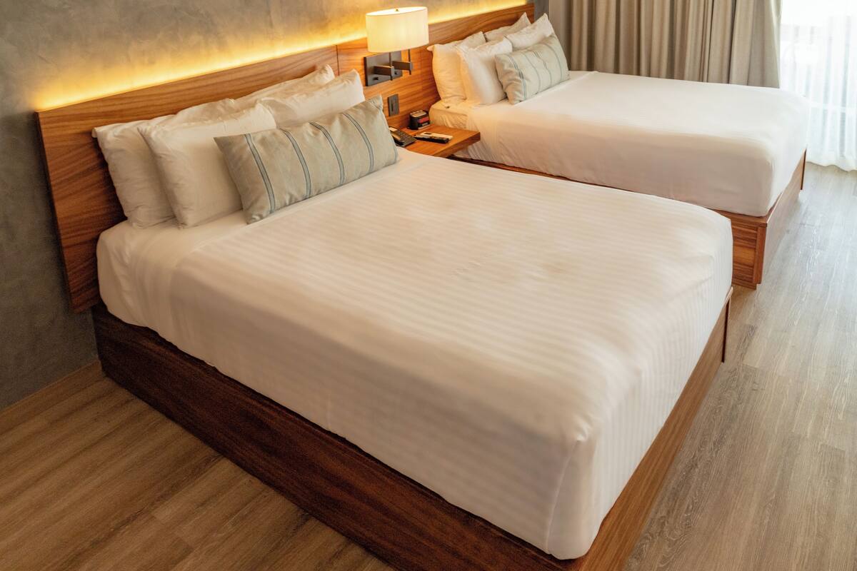 A double bed with a wooden frame and a headboard with integrated lighting. There is a nightstand with a lamp and a remote control.