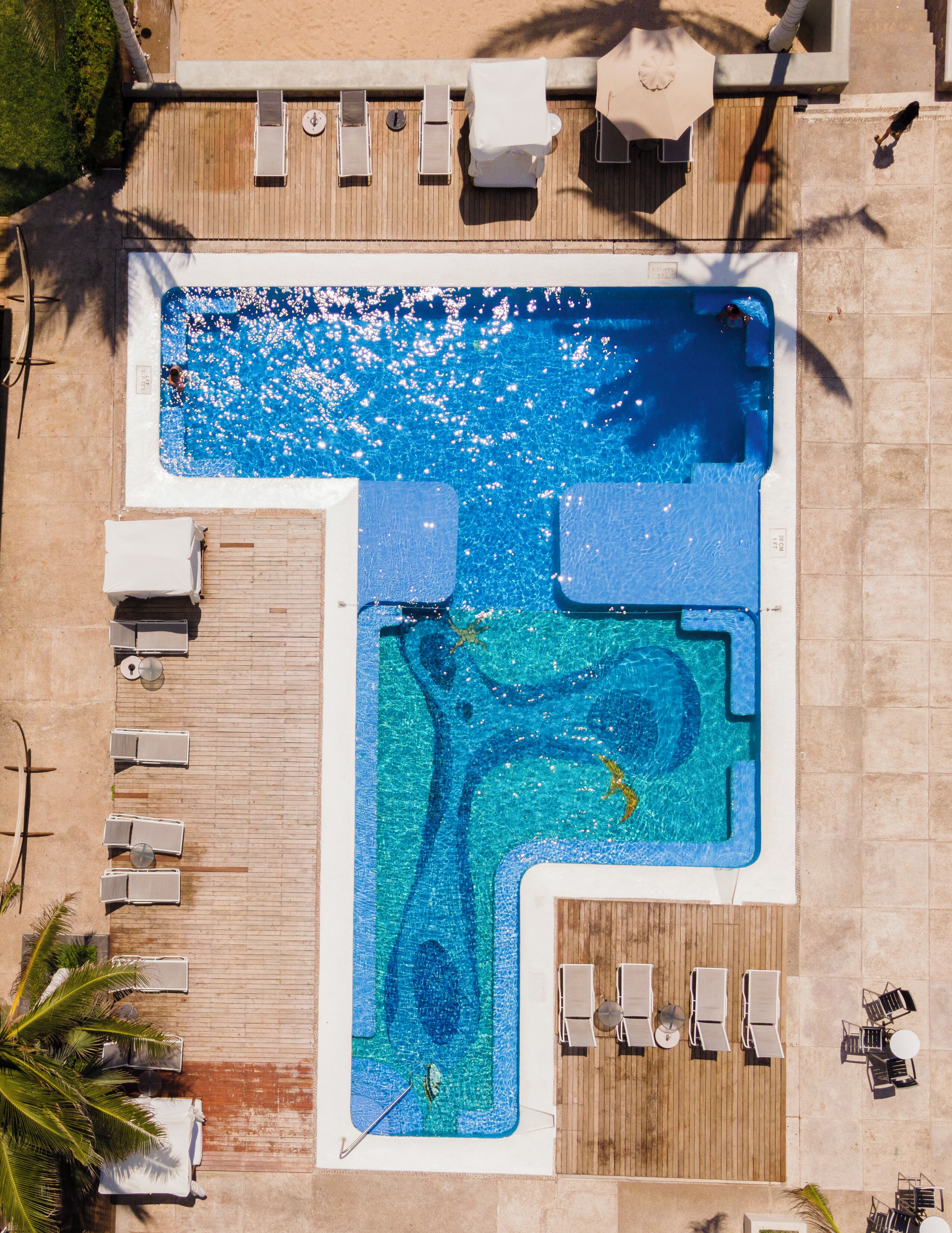A rooftop pool with a wooden deck, lounge chairs, and a small waterfall feature.