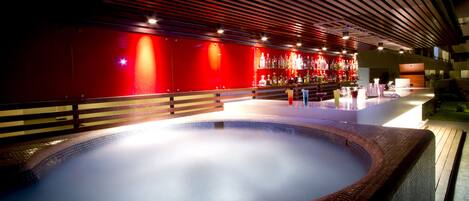 A hot tub area with a tiled floor, wooden railings, and a red wall with a bar in the background.