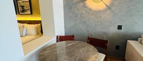 Un espace repas comprenant une table ronde en marbre, des chaises en bois et un luminaire moderne au plafond.