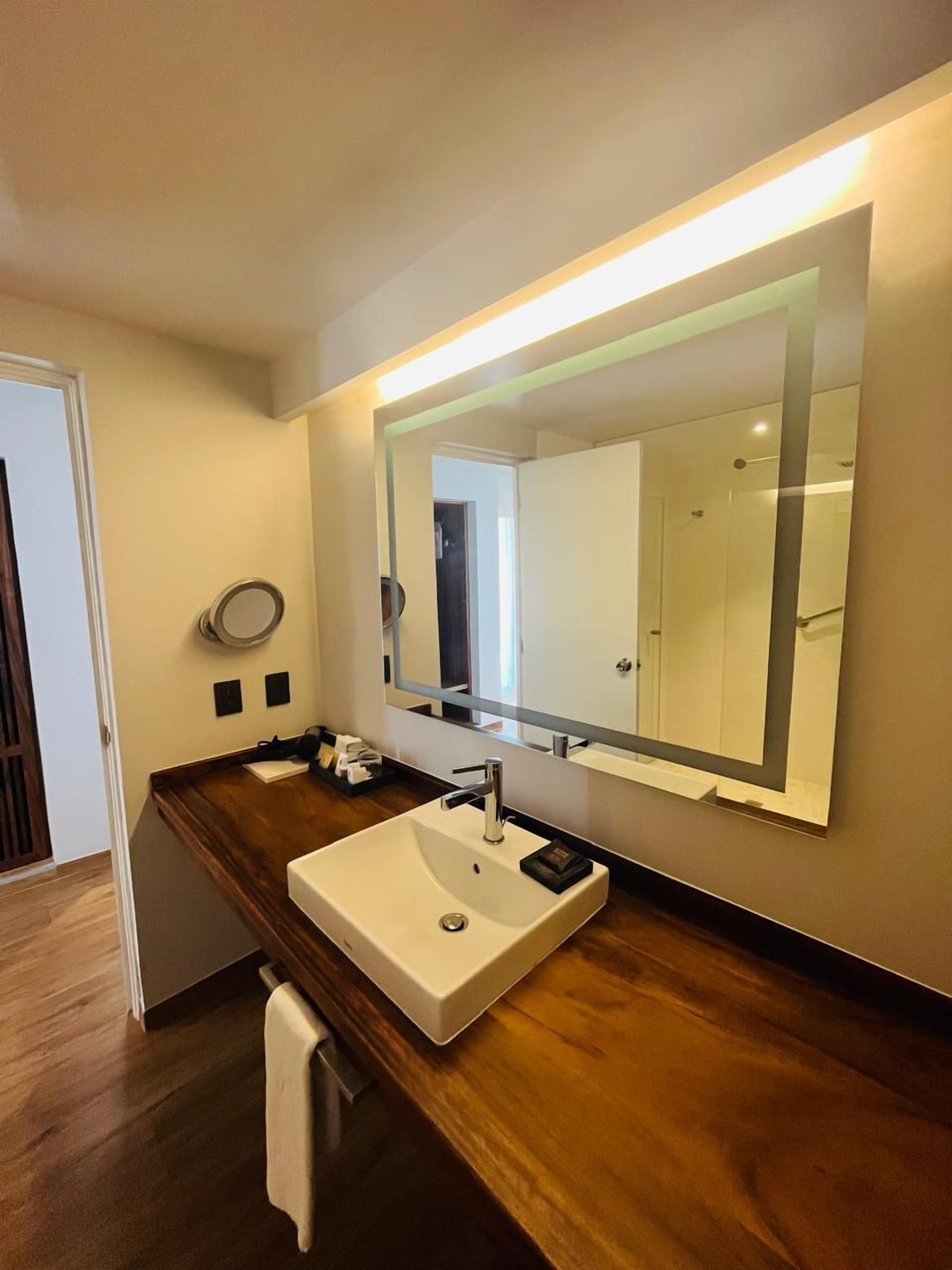 Une salle de bain moderne avec un grand miroir, un lavabo blanc et un plan de travail en bois.