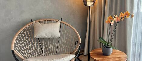 A wicker chair with a cushion, a floor lamp, and a small table with a potted plant.