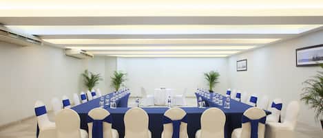 A conference room with a long table, white chairs with blue sashes, and potted plants.