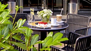 A round table with chairs, a glass of water, a white cup, and a plate with food and flowers at the Park Hotel entrance. - Seaside Park Hotel Leipzig (Leipzig)
