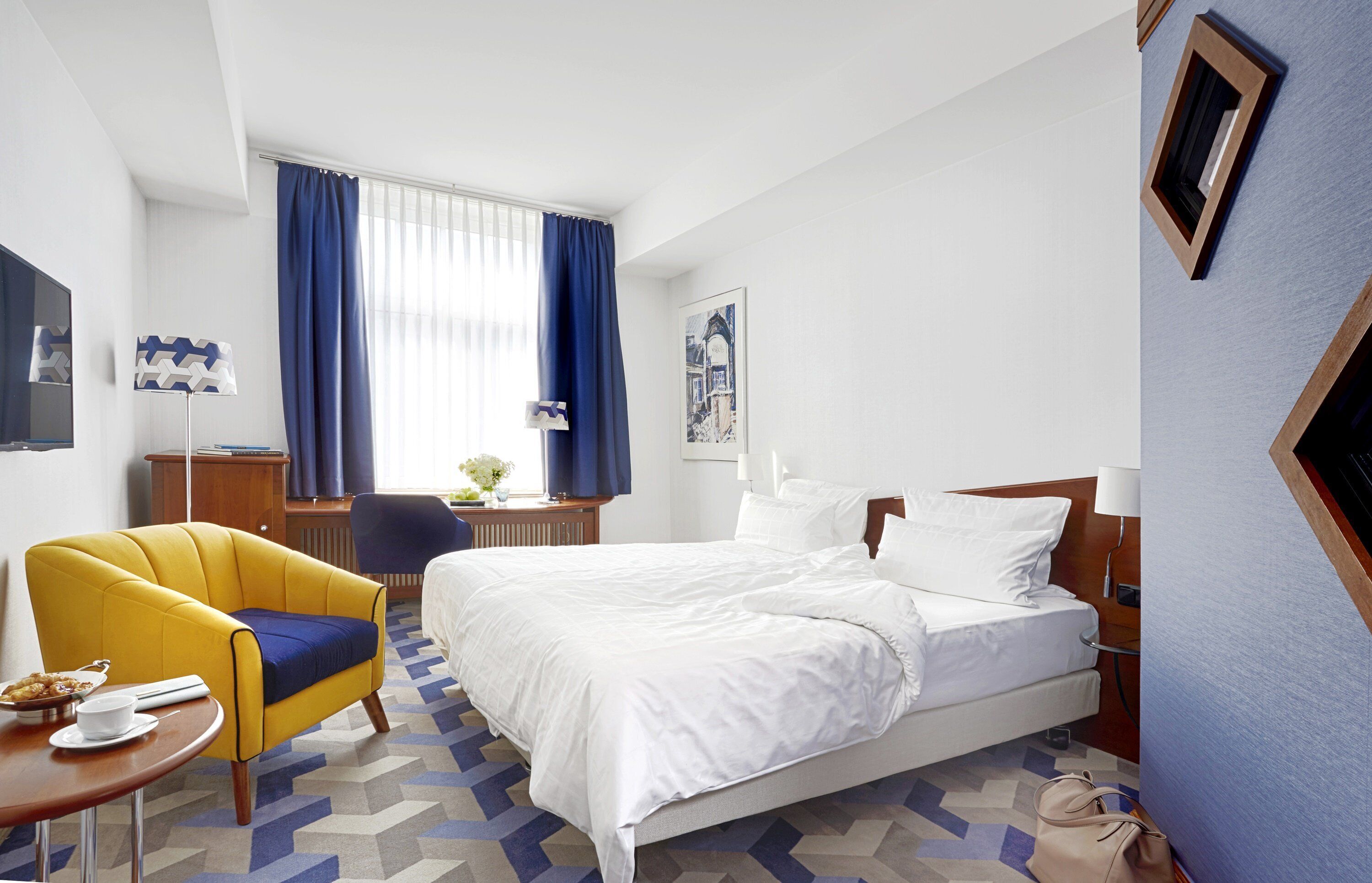 A hotel room with a bed, a desk, a chair, and a small table.