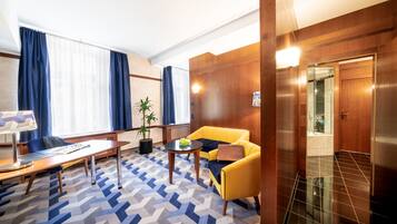 A hotel room with a wooden panel wall, a yellow sofa, a wooden desk, and a patterned carpet.