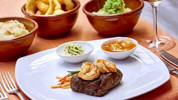 Ein Teller mit Steak und Garnelen, dazu Krautsalat, eine cremige Soße und eine Schüssel Pommes.