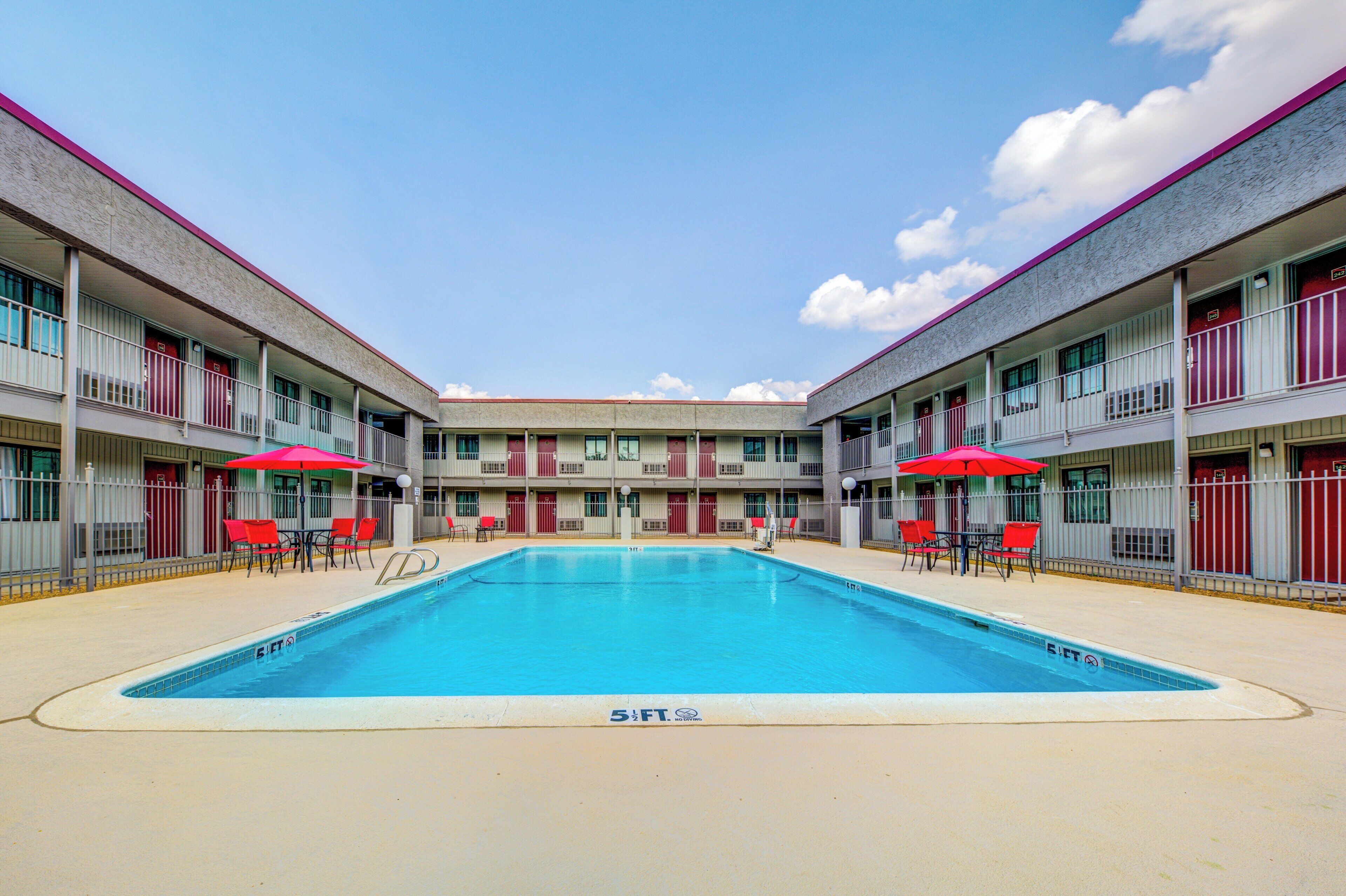 Una piscina con una profundidad de 1,7 metros, rodeada por un edificio con balcones y sillas rojas.