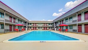 A swimming pool with a 5½ ft depth, surrounded by a building with balconies and red chairs. - Red Roof Inn Lewisville (Lewisville)