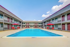 A swimming pool with a 5½ ft depth, surrounded by a building with balconies and red chairs. - Red Roof Inn Lewisville (Lewisville)