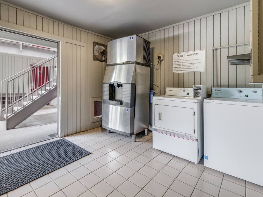 A laundry area with a Whirlpool washer and dryer, a stainless steel refrigerator, and a sign indicating guest laundry rules.