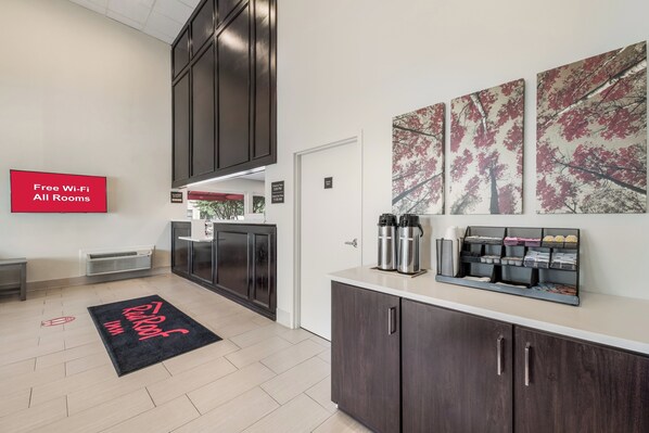 A modern hotel lobby with a reception desk, a coffee station, and artwork on the walls.
