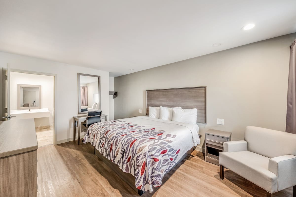A modern hotel room with a large bed, a desk, a chair, and a nightstand.