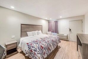 A modern hotel room with a large bed, bedside tables, a desk, and a built-in air conditioning unit.