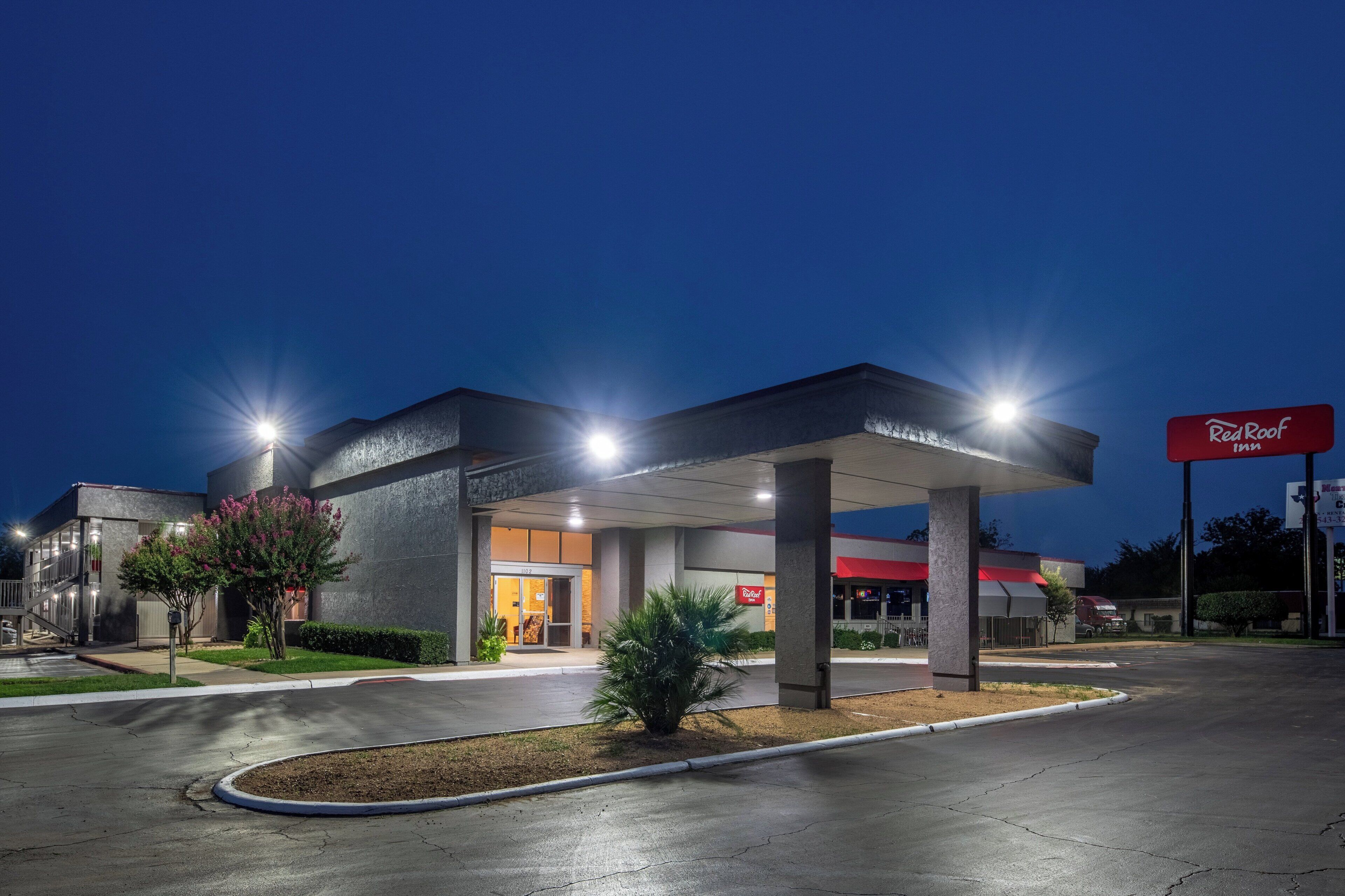 A Red Roof Inn with a covered parking area, a well-lit entrance, and a clear sky at dusk.