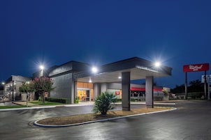 A Red Roof Inn with a covered parking area, a well-lit entrance, and a clear sky at dusk.
