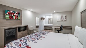 Ein Hotelzimmer mit Bett, Schreibtisch, Stuhl, Fernseher, Mikrowelle und Spiegel im Badezimmer.