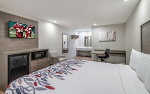 A hotel room with a bed, a desk, a chair, a TV, a microwave, and a bathroom mirror. - Red Roof Inn Lewisville (Lewisville)