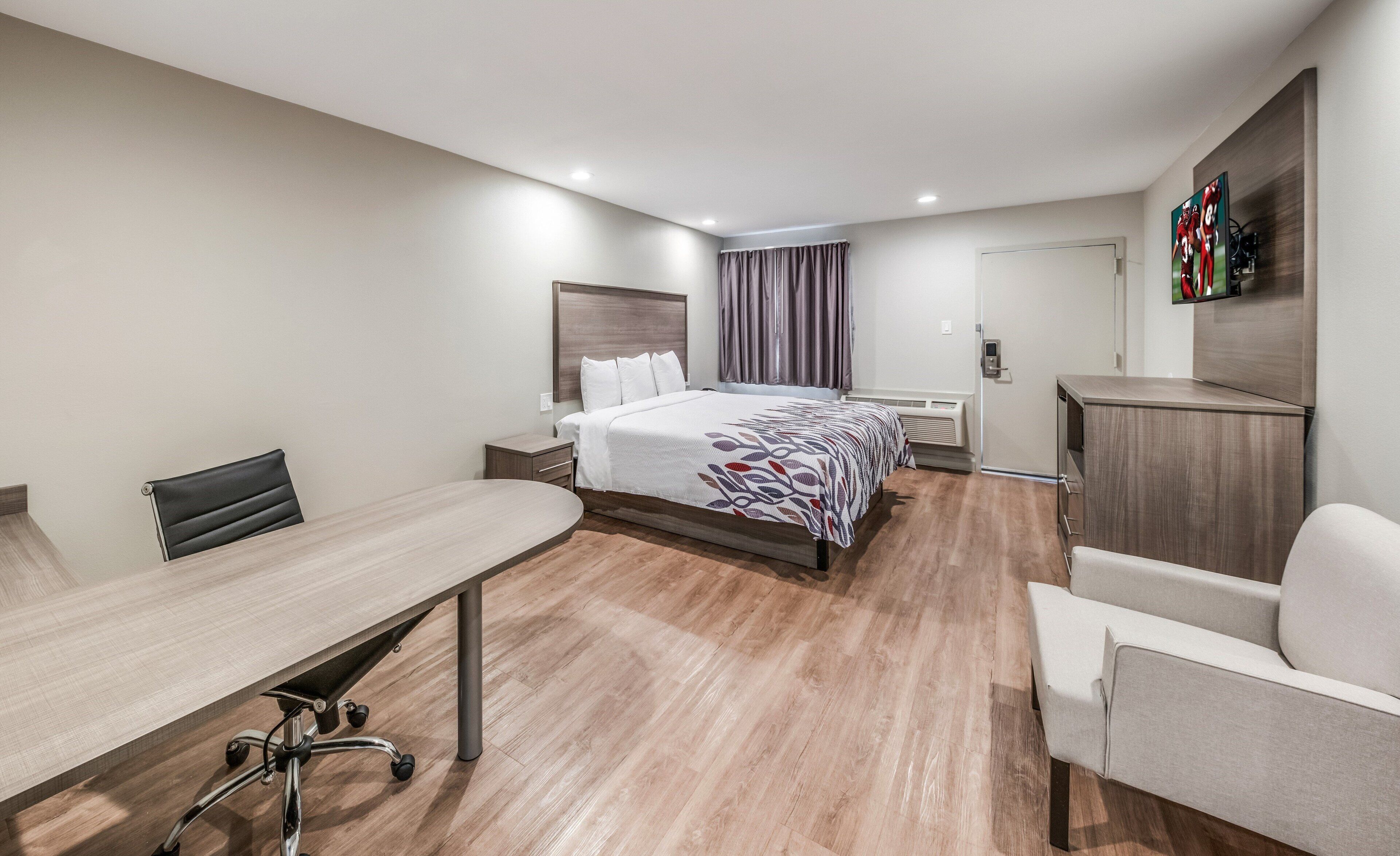 A hotel room with a bed, a desk, a chair, a TV, and a wardrobe.