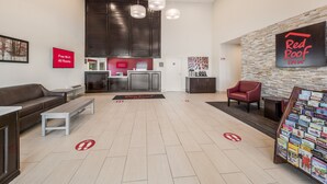 A hotel lobby with a reception desk, a sofa, a coffee table, and a Red Roof Inn sign. - Red Roof Inn Lewisville (Lewisville)