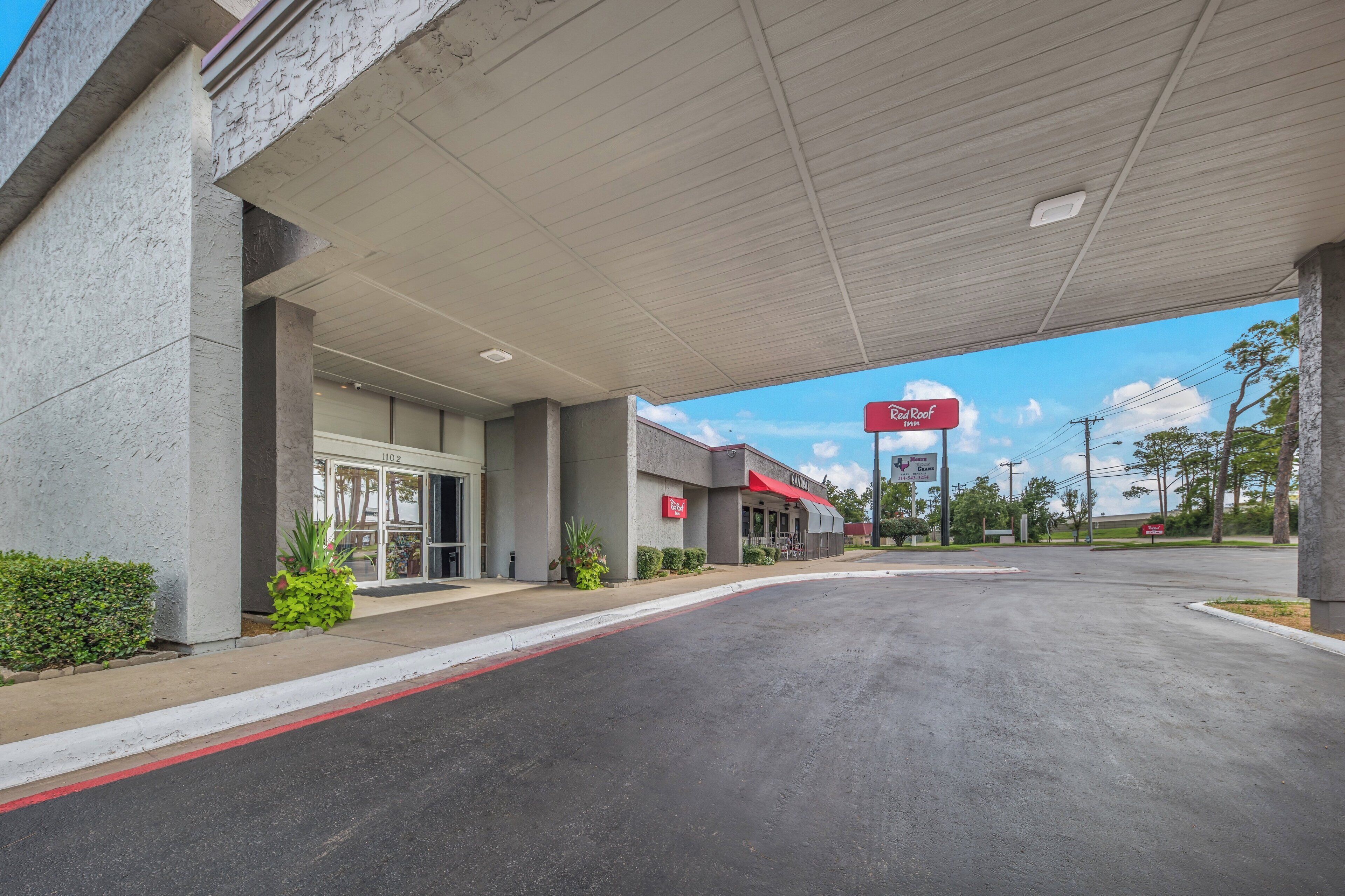 Un hotel Red Roof Inn con área de estacionamiento techada y cielo despejado.