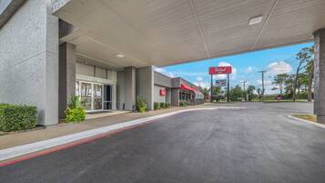 Un hotel Red Roof Inn con área de estacionamiento techada y cielo despejado.