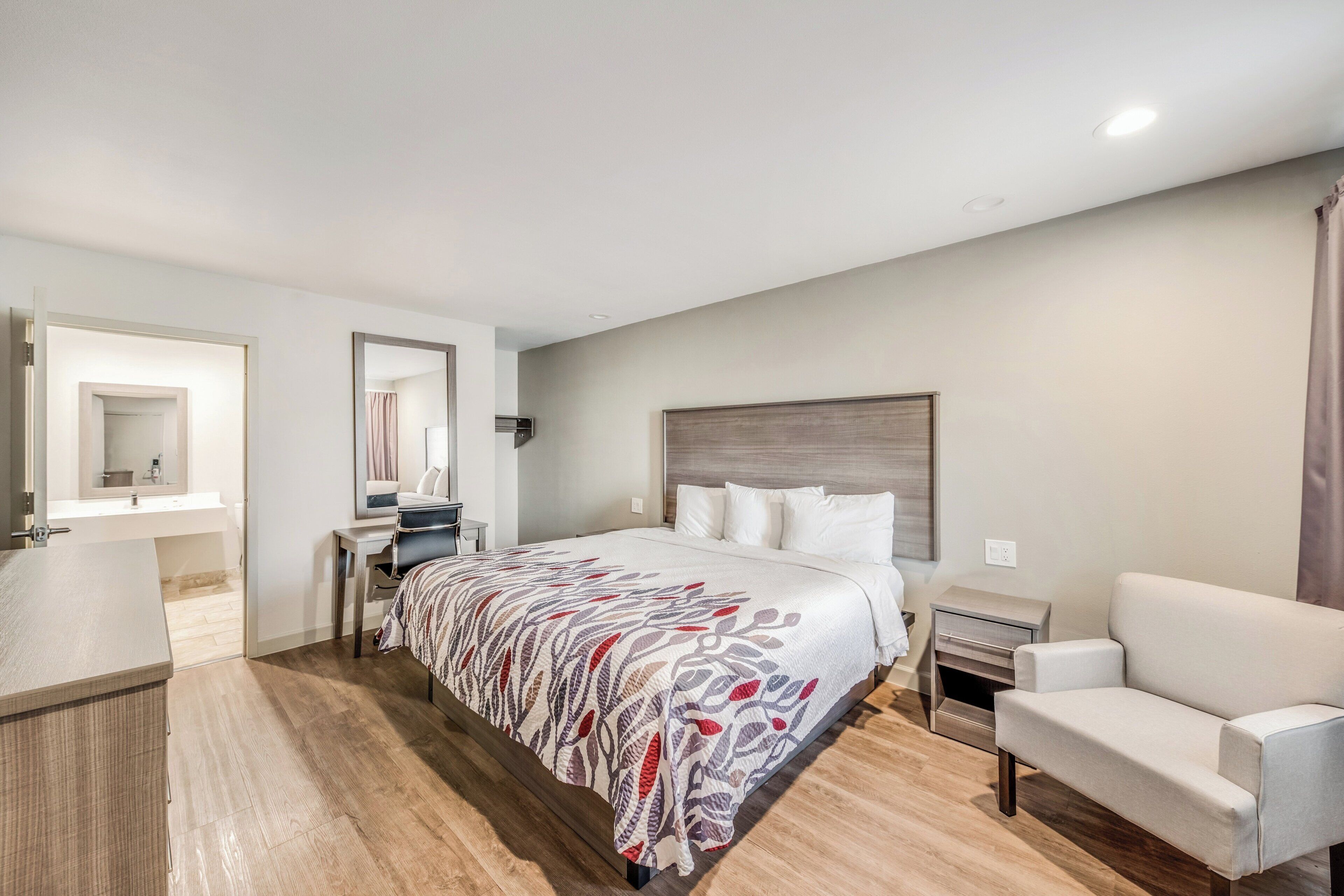Una habitación de hotel con cama, escritorio, silla y mesita de noche.