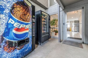 Máquina automática de vendas com logotipo da Pepsi, entrada com porta de vidro e uma planta em vaso no interior.
