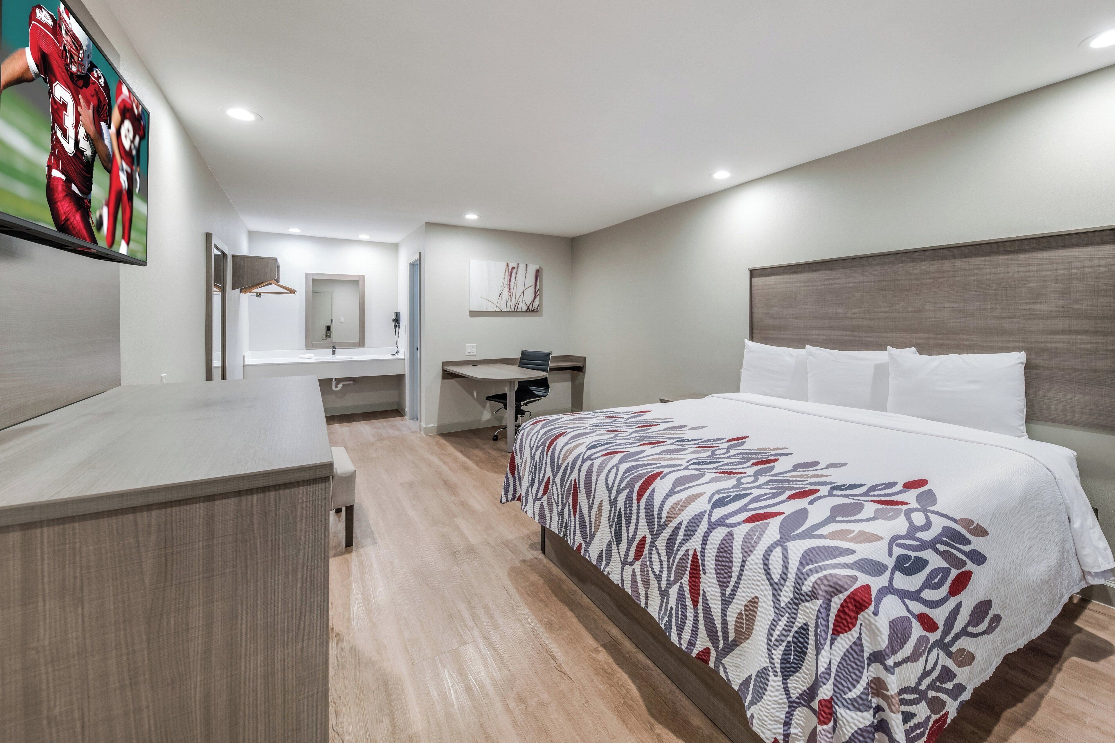 Ein Hotelzimmer mit Bett, Schreibtisch, Stuhl, Fernseher und Bad.