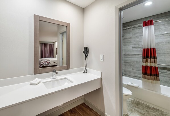 A modern bathroom with a white sink, a mirror, and a shower curtain. - Red Roof Inn Lewisville (Lewisville)