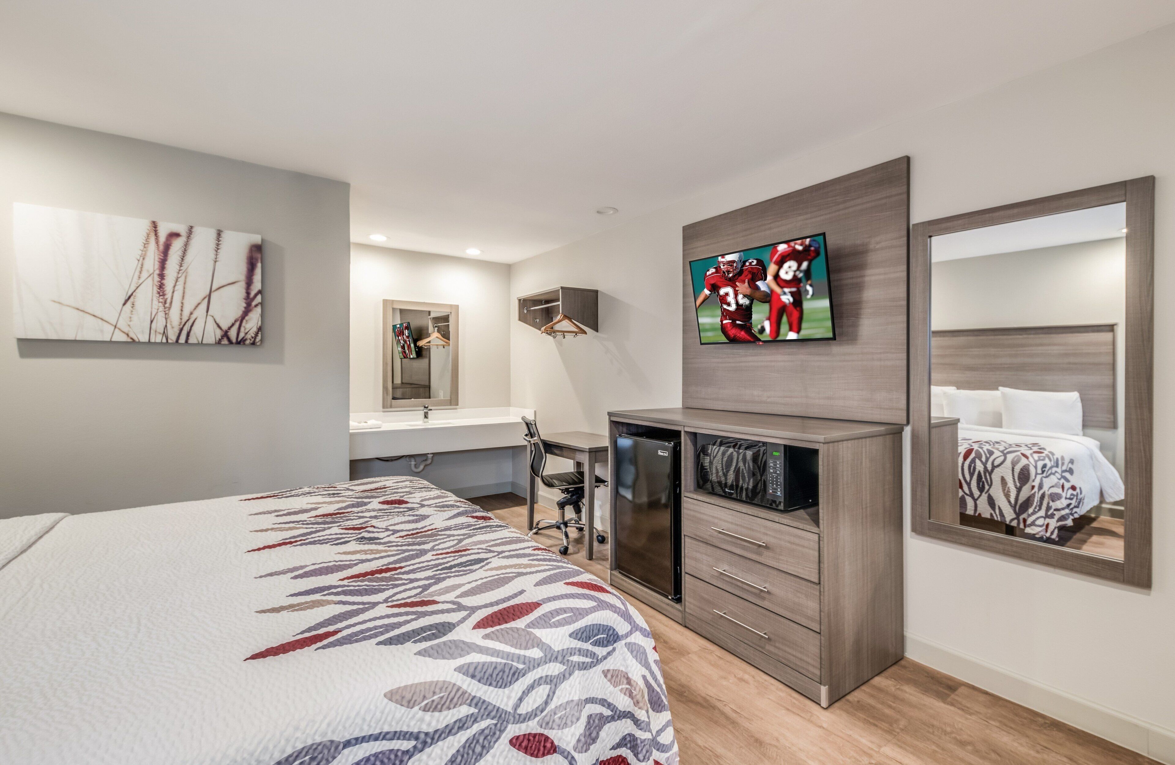 Una habitación de hotel moderna con una cama, un escritorio, un espejo y un televisor.