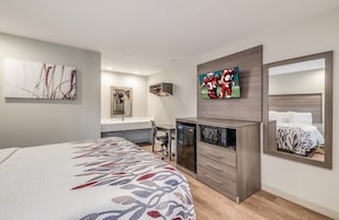 A modern hotel room with a bed, a desk, a mirror, and a TV.