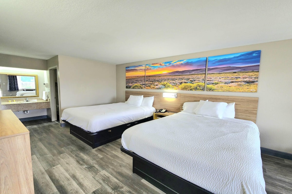 A hotel room with two beds, a bathroom, and a large landscape painting on the wall.