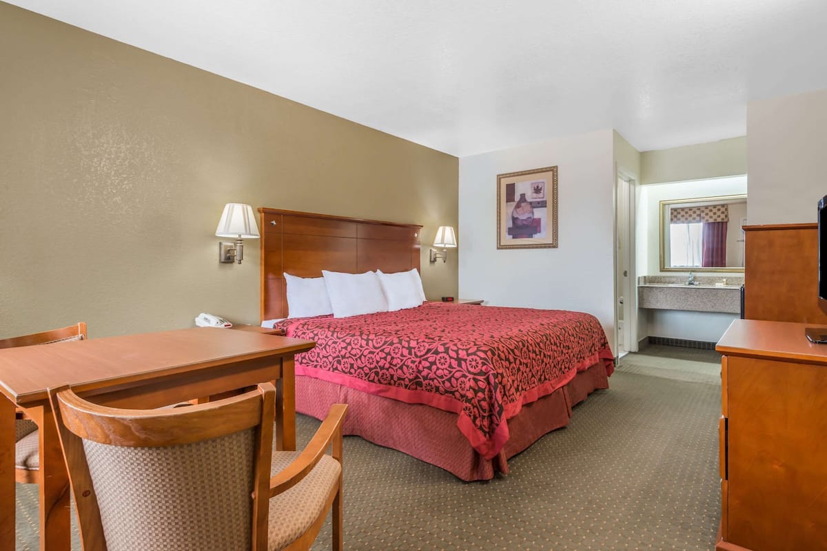 A hotel room with a bed, a desk, a chair, a lamp, and a mirror.