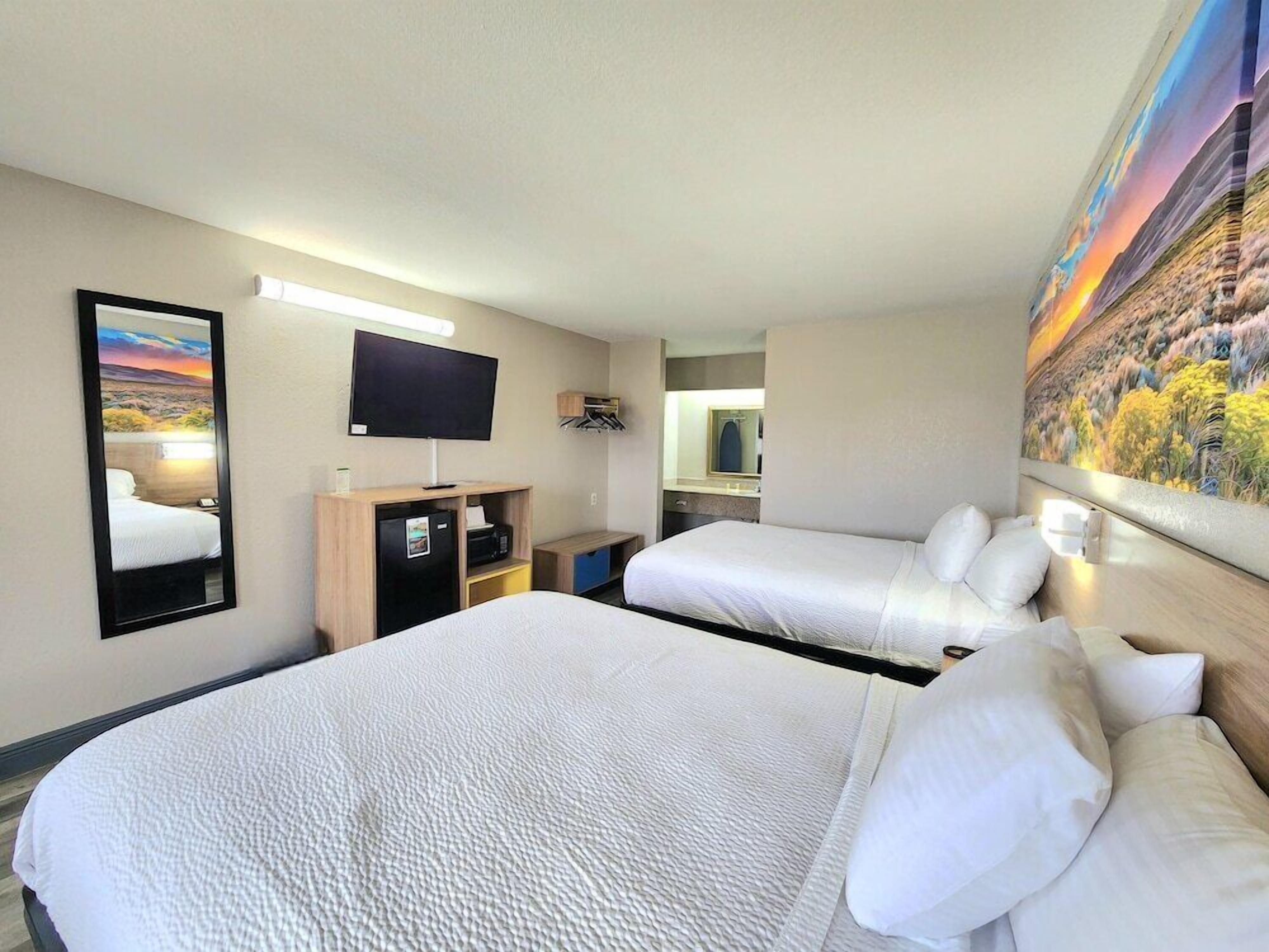A hotel room with two beds, a flat-screen TV, a desk with a computer, a mirror, and a painting on the wall.
