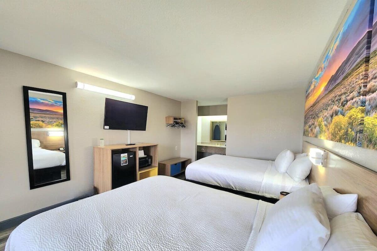 A hotel room with two beds, a flat-screen TV, a desk with a computer, a mirror, and a painting on the wall.