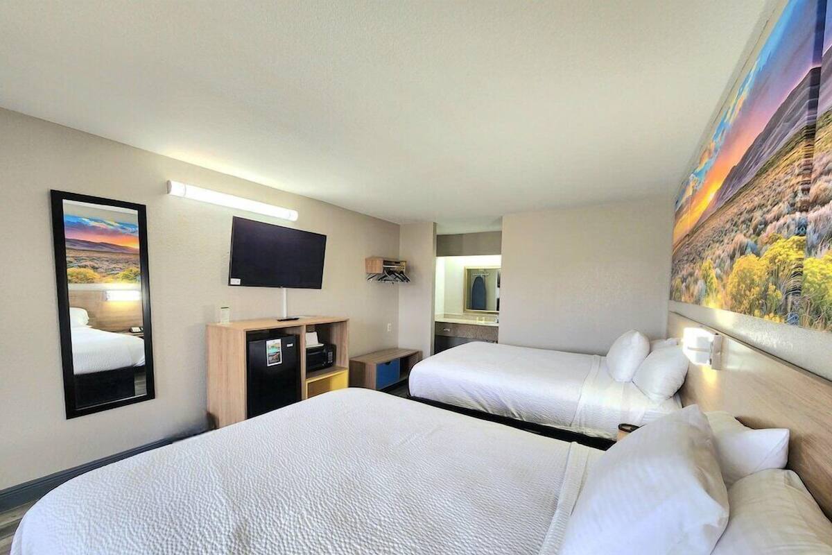 A hotel room with two beds, a flat-screen TV, a desk with a computer, a mirror, and a painting on the wall.