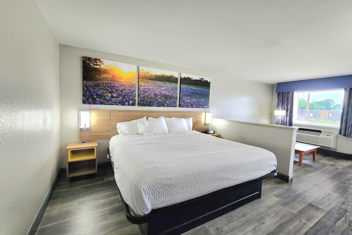 A hotel room with a large bed, a nightstand, a desk, and a window with curtains.