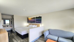 Habitación de hotel con cama, sofá, mesa de madera, espejo, lavamanos y una obra de arte colgada en la pared.