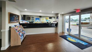 Zona de recepción con mostrador, obras de arte enmarcadas, carteles informativos y un atril de madera para revistas.