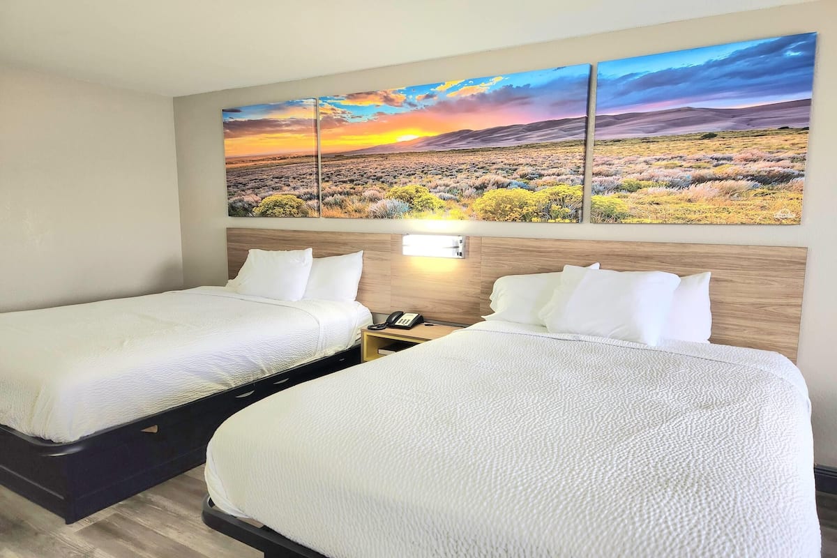 A hotel room with two beds, a nightstand with a phone, and a large landscape painting above the beds.