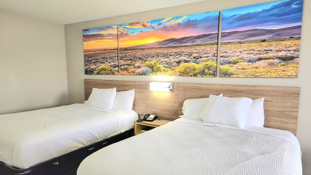 Una habitación de hotel con dos camas, un cabecero de madera, una mesita de noche con un teléfono y un cuadro de paisaje grande sobre las camas.