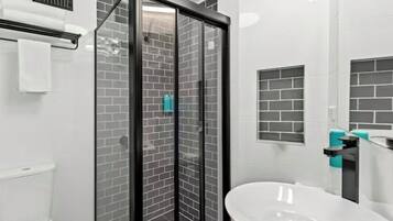 Un baño moderno con ducha envuelta en vidrio, un lavamanos blanco y un inodoro.