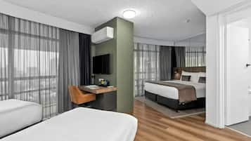 A hotel room with a bed, a desk with a chair, a TV, and a large window with curtains.
