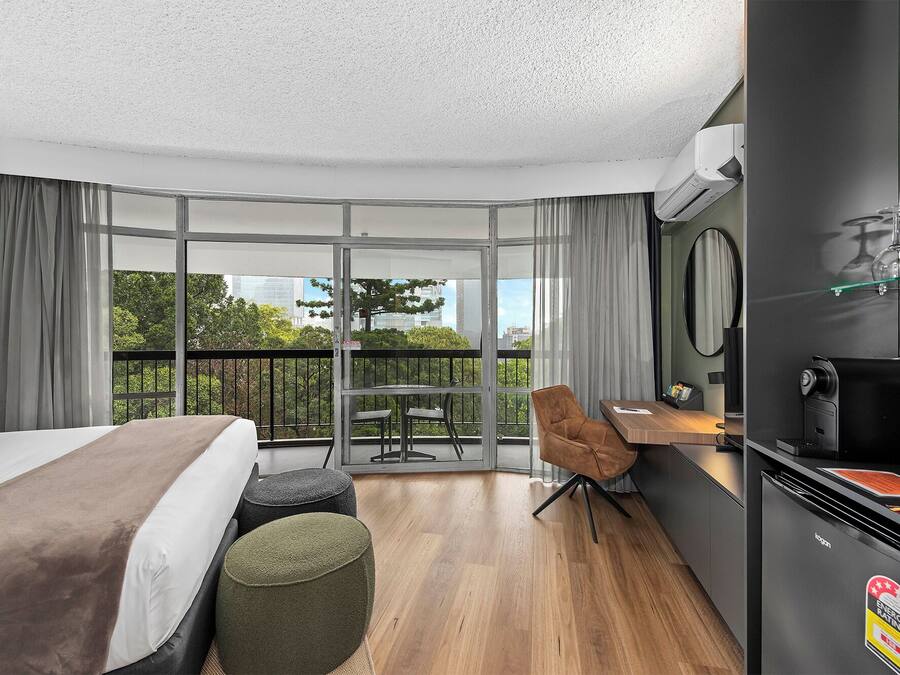 Habitación de hotel moderna con una cama grande, una mesita, una silla, un balcón con vistas a la ciudad y una kitchenette.