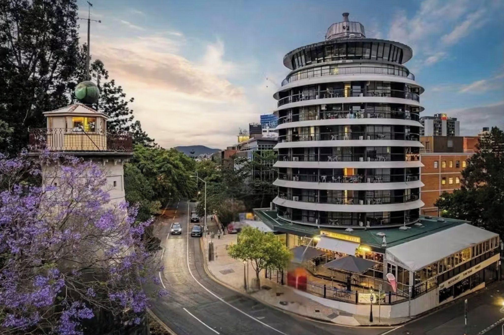 A multi-story hotel with a circular design, located near a road with vehicles.