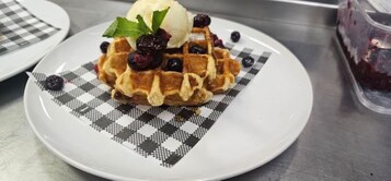 A waffle with blueberries and a scoop of ice cream on a checkered plate.