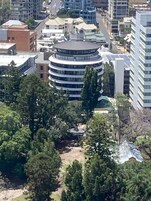 A multi-story building with a circular central section, surrounded by trees and other buildings.